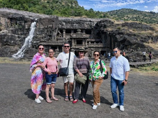 Groupe de touristes posant devant les grottes rupestres d'Ajanta et une cascade.