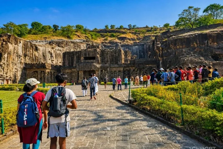 Des touristes se dirigent vers l'impressionnante façade rupestre des grottes d'Ajanta par une journée ensoleillée.