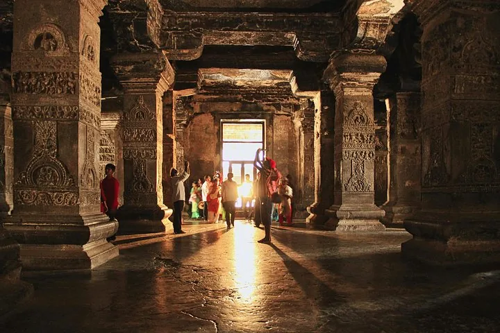 Des touristes explorent l’intérieur faiblement éclairé et à piliers d’une grotte à Ajanta.